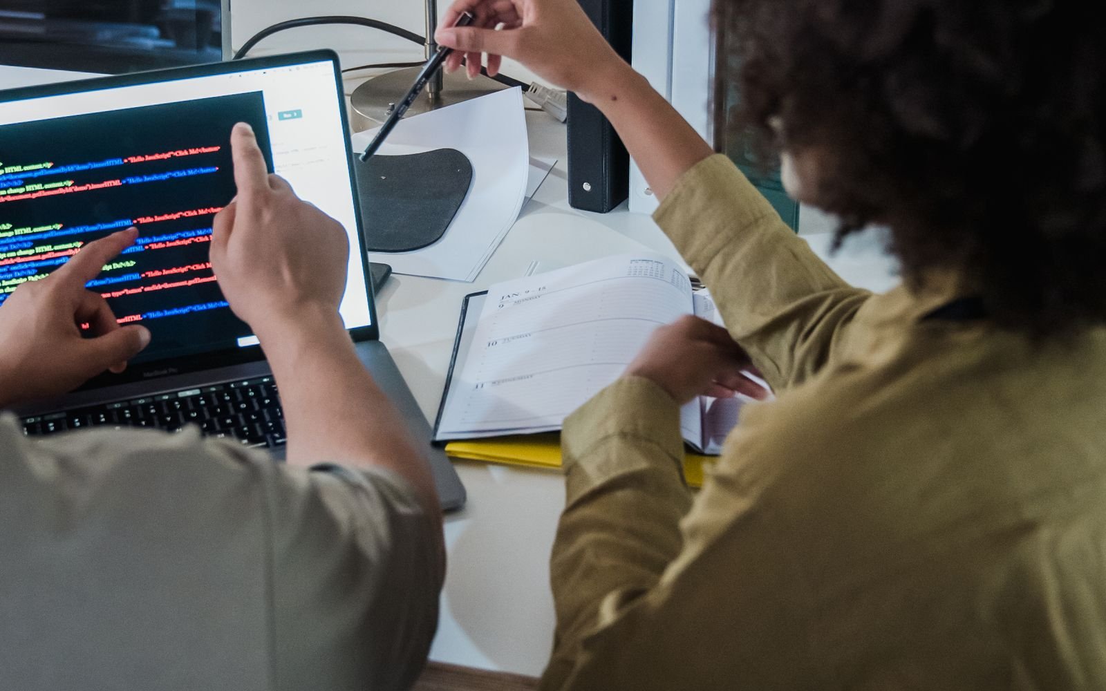 Dos personas comentando el código sobre un portátil en una mesa de trabajo